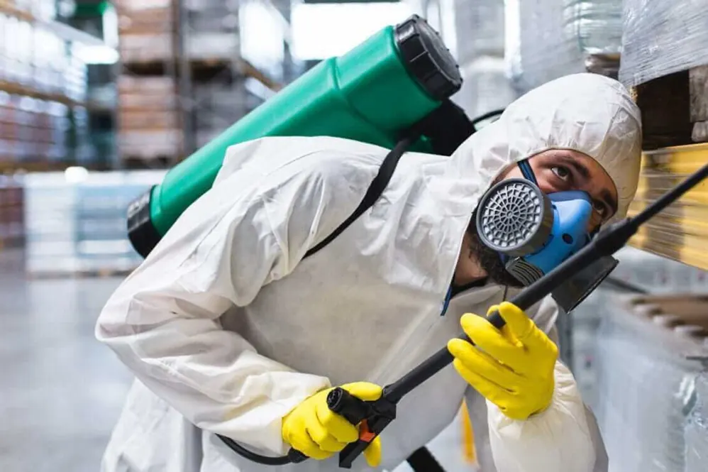 Técnico con máscara y traje de protección aplicando un tratamiento en un depósito